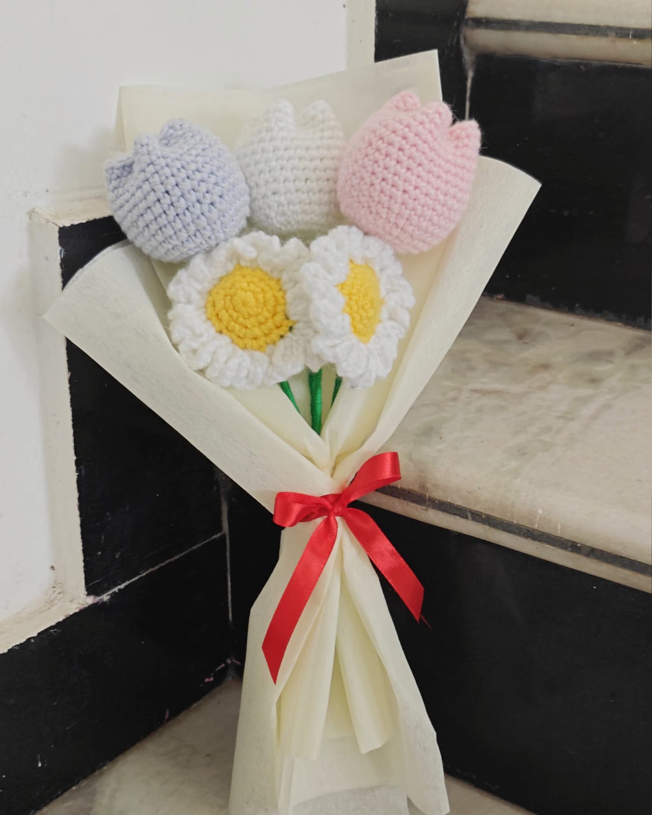 Bouquet of crocheted flowers with a red ribbon on a white background