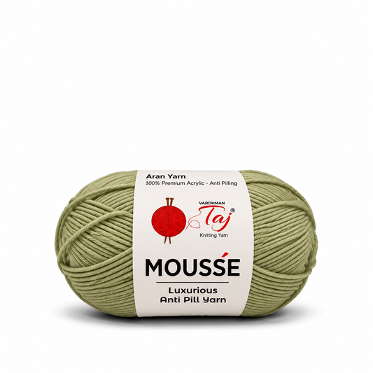 A ball of Moussé Aran yarn in a muted sage green color, featuring a white paper label with the brand 'Yardham Taj' and product details.