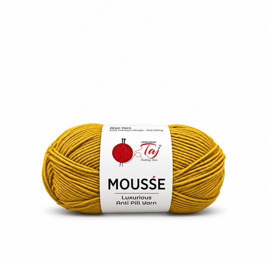 A single skein of yarn in a mustard yellow color with a white paper label. The label features the brand 'Taj' and the product name 'MOUSSE' with 'Luxurious Anti Pill Varn' written below.