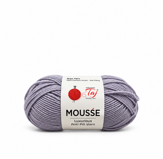 A skein of lavender-gray yarn with a white paper label that reads 'Mousse Luxurious Anti Pill Wool' by Taj Fabrics, on a solid white background.